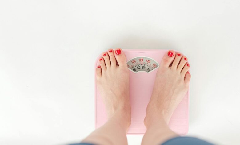 Top view of crop anonymous barefoot female measuring weight on scales on white background